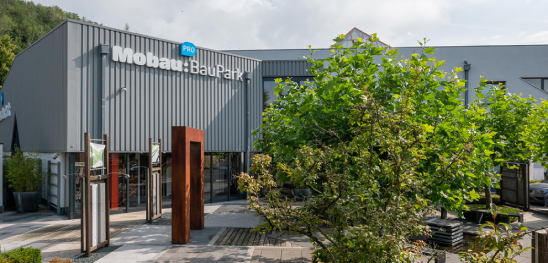 Gebäude in Mönchengladbach mit Blau weissem Bobau Baupark Logo am Gebäude und vielen grünen Bäumen im Vordergrund