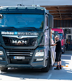 grauer LKW vor dem Lager mit Mobau-Mitarbeiter