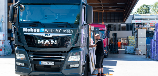 Schwarzer LKW mit Blau weissem Mobau Wirtz & Classen Logo und schwarz gekleidetem Mitarbeiter bei der Verladung von Ware