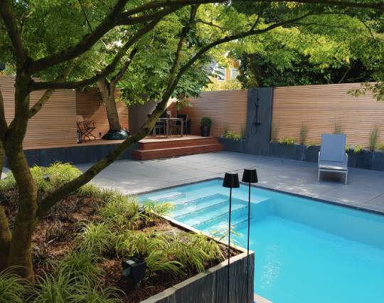 graue natursteinplatten, mit pool und ein beet voller erde mit einem baum 